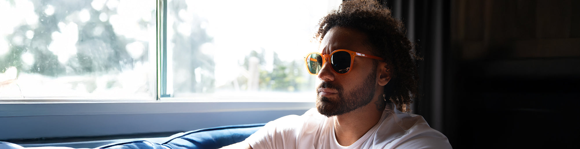 male model sitting by the window wearing orange sunglasses