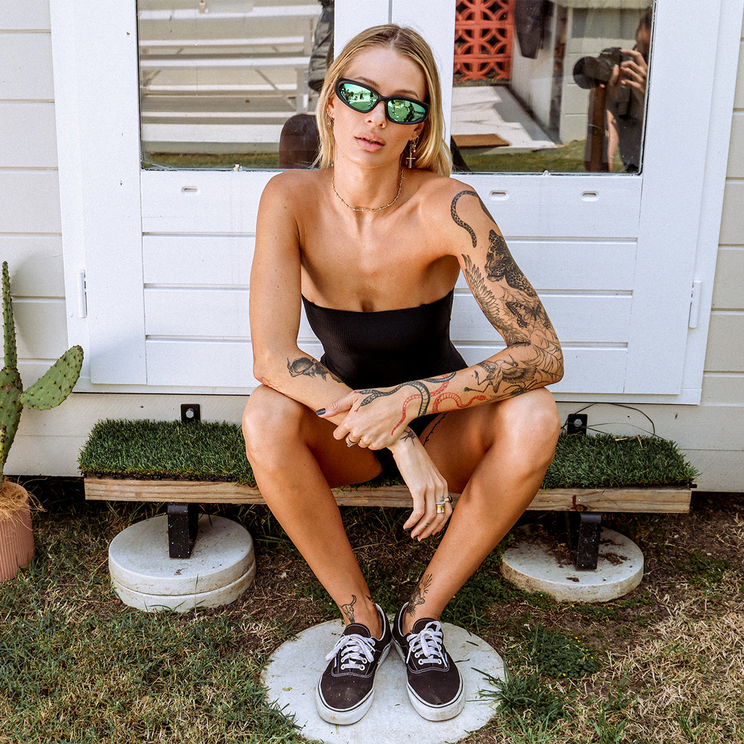 Reefer Polarised Black and Green Wrap Around Sunglasses made of recycled plastic on female model sitting on stair