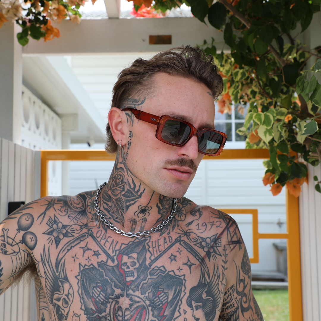 Rocker Polarised Brown Rectangle Sunglasses on a male model next to a house
