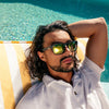 Spartan Recycled Black Rectangle Sunglasses with gold matte lens on a male model lying on a pool chair