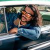 Vespa II Recycled Square Sunglasses with Black Frame and Red Matte lens on a male model leaning out of a classic car