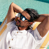 Vespa II Recycled Square Sunglasses with Black Frame and Silver Matte lens on a male model in pool chair looking up