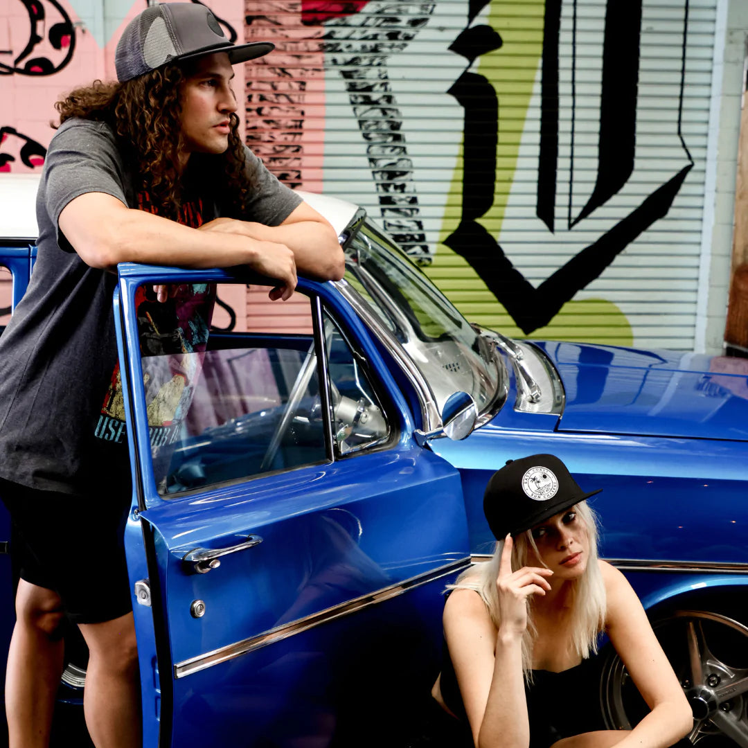 Rubber Badge Grey Cap side view on a male model leaning on a classic car