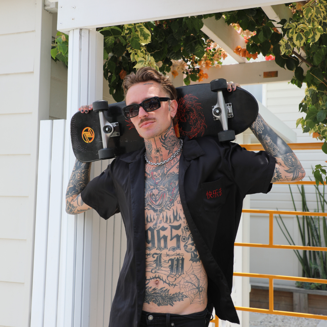 Rocker Polarised Black Rectangle Sunglasses on a male model holding a skateboard next to a house